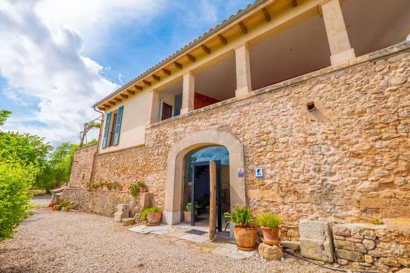 A stone building exterior has an arched entrance and an upper covered terrace.
