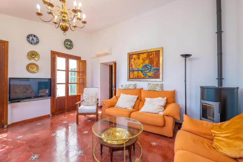 A bright living room with orange seating, a glass coffee table, and a framed painting.