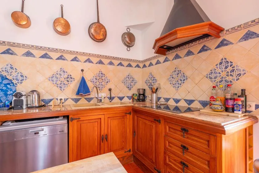 A tiled kitchen with wooden cabinets, countertop appliances, and cookware hanging on the wall.