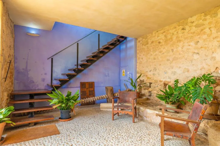A stone-walled interior with a staircase, seating, and potted plants.