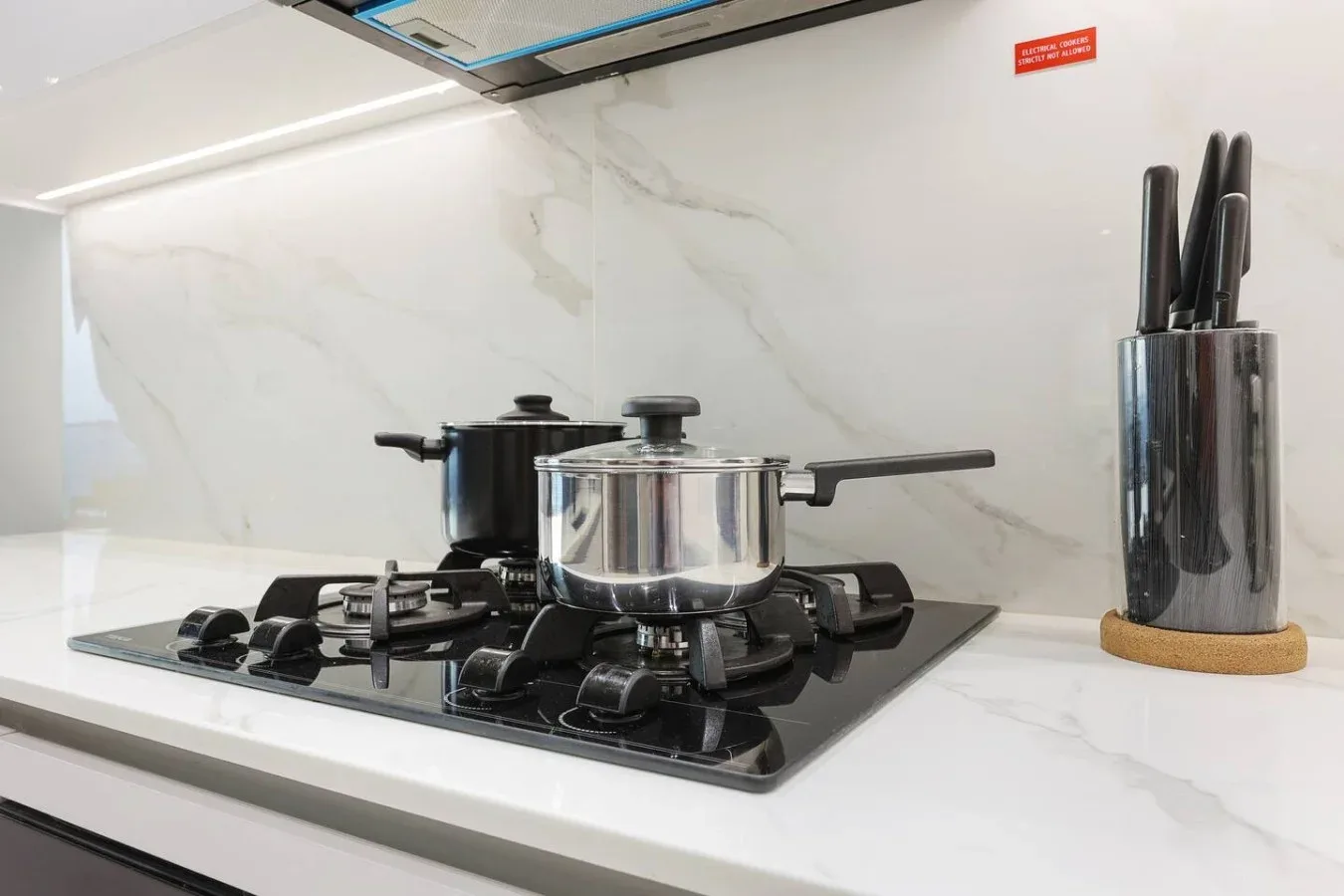 Una placa de cocina con ollas y un bloque de cuchillos sobre la encimera.