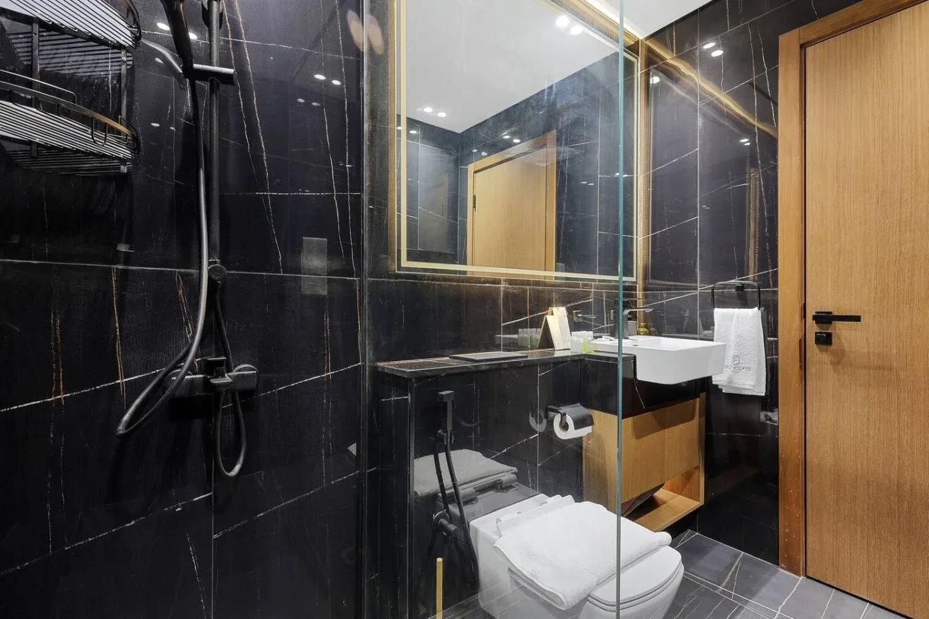 Un baño moderno con ducha de vidrio, lavabo y paredes de azulejos oscuros.