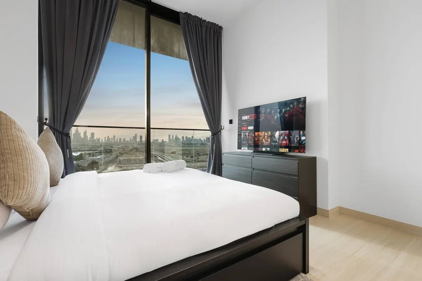 Un dormitorio con una cama junto a una ventana alta con vistas al perfil urbano.