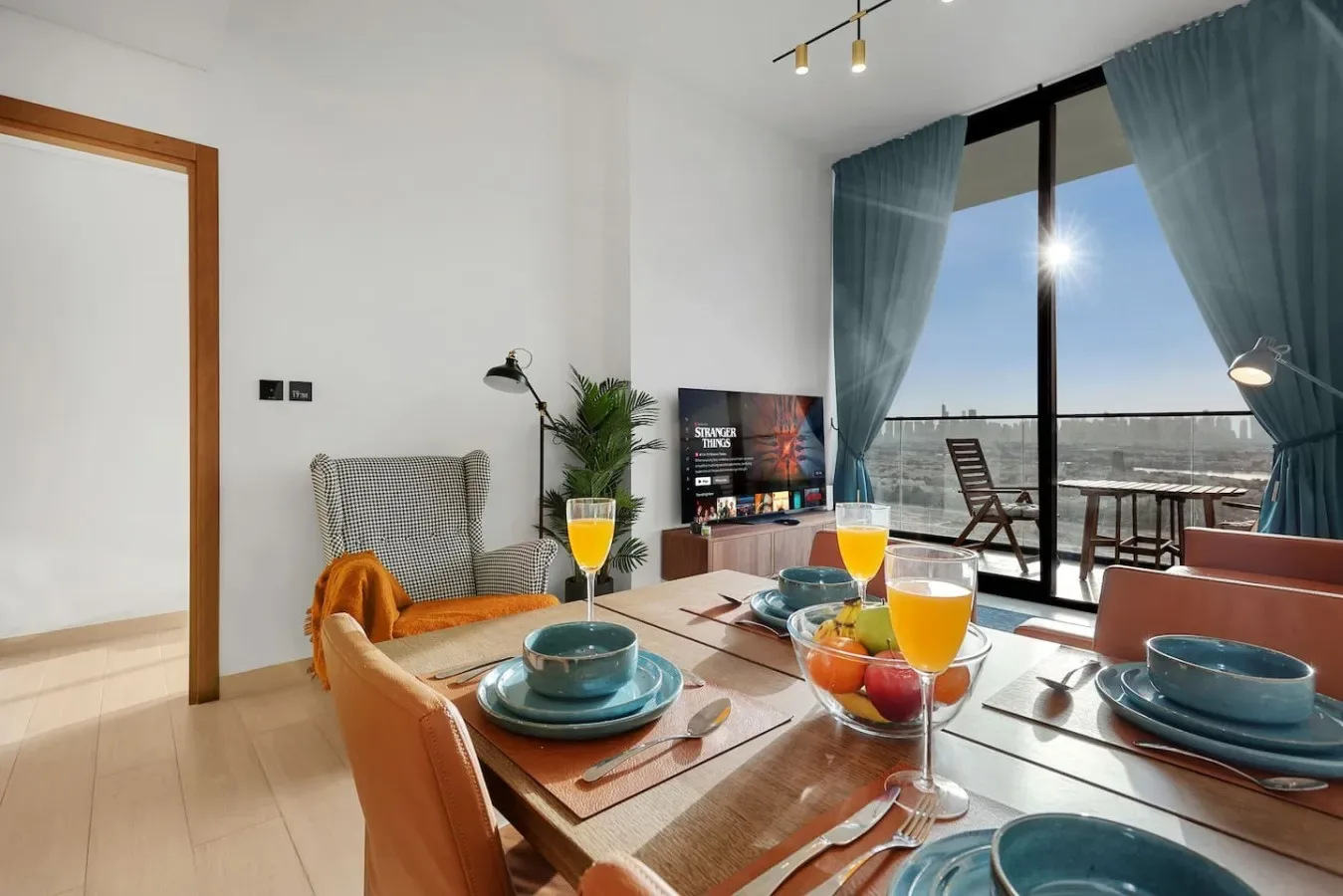 Un comedor luminoso con la mesa puesta junto a grandes ventanales y cortinas turquesas.