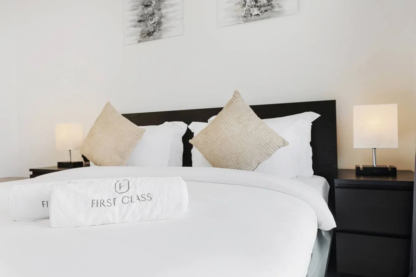 Una cama bien tendida con ropa de cama blanca, cojines decorativos y lámparas de noche.