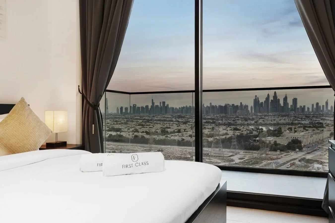 Un dormitorio con una cama junto a ventanales con vistas al perfil urbano.