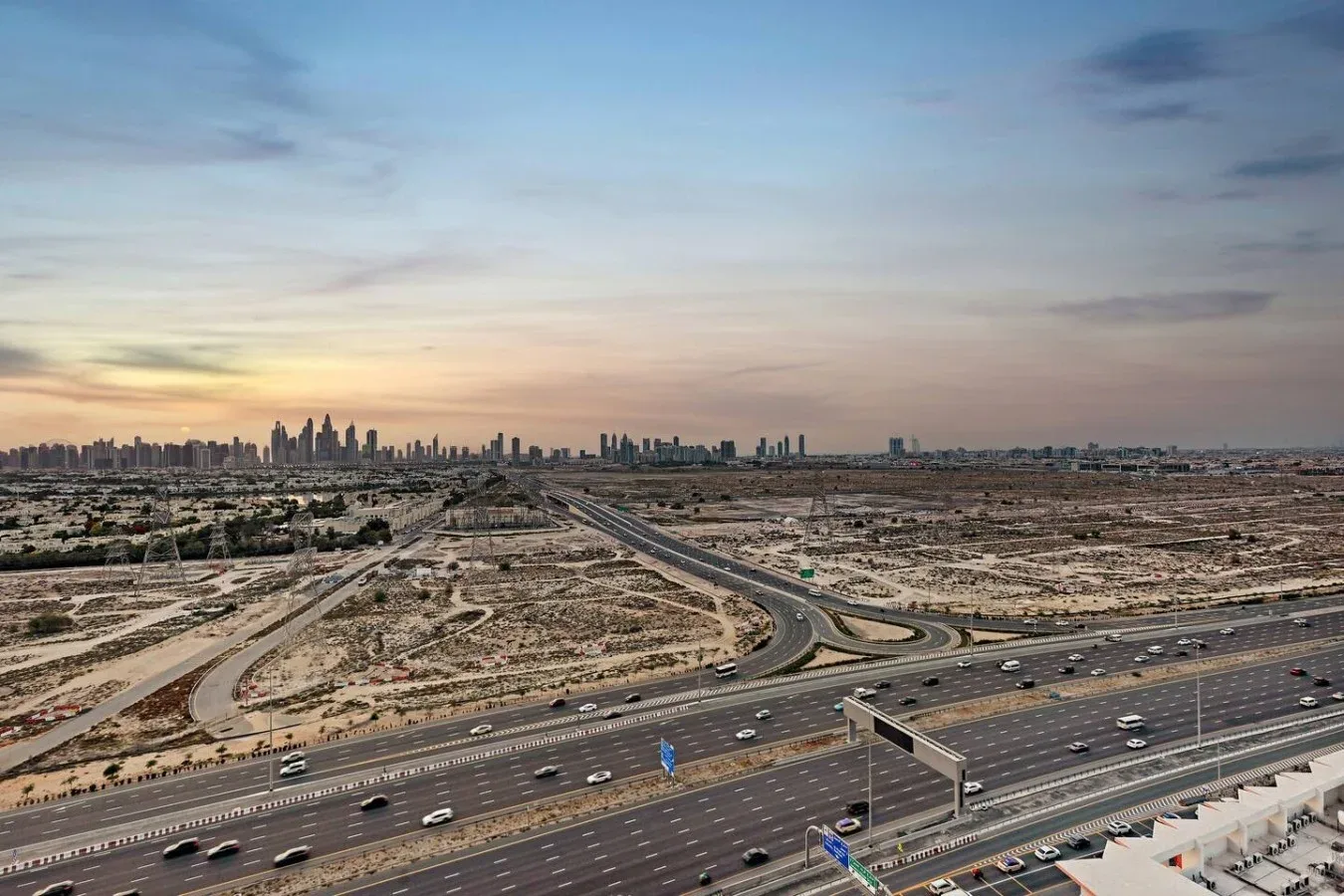 Un horizonte urbano se alza tras un amplio enlace de autopistas bajo un cielo colorido.