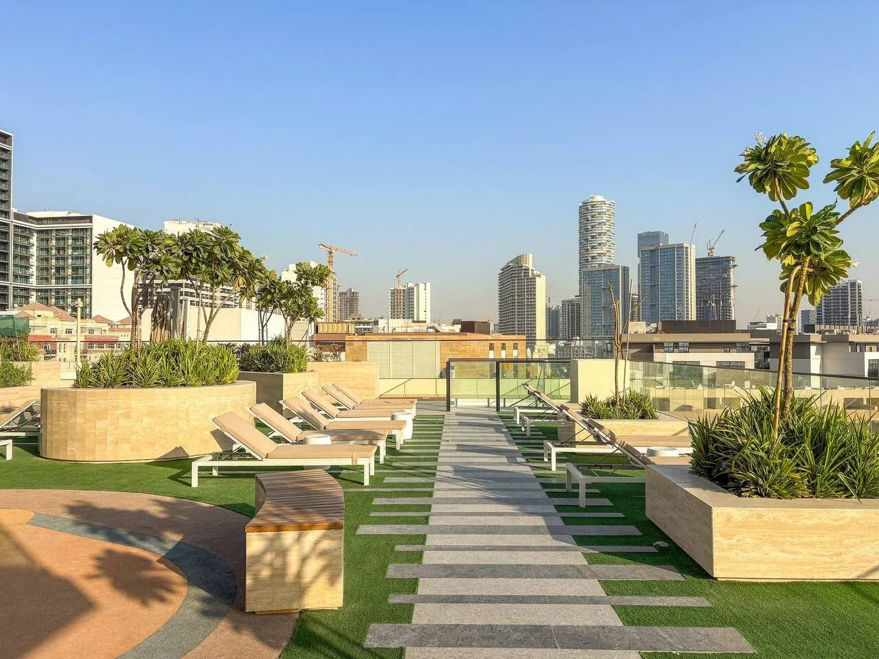 Una terraza en la azotea tiene un sendero pavimentado, asientos, jardineras y un horizonte urbano.