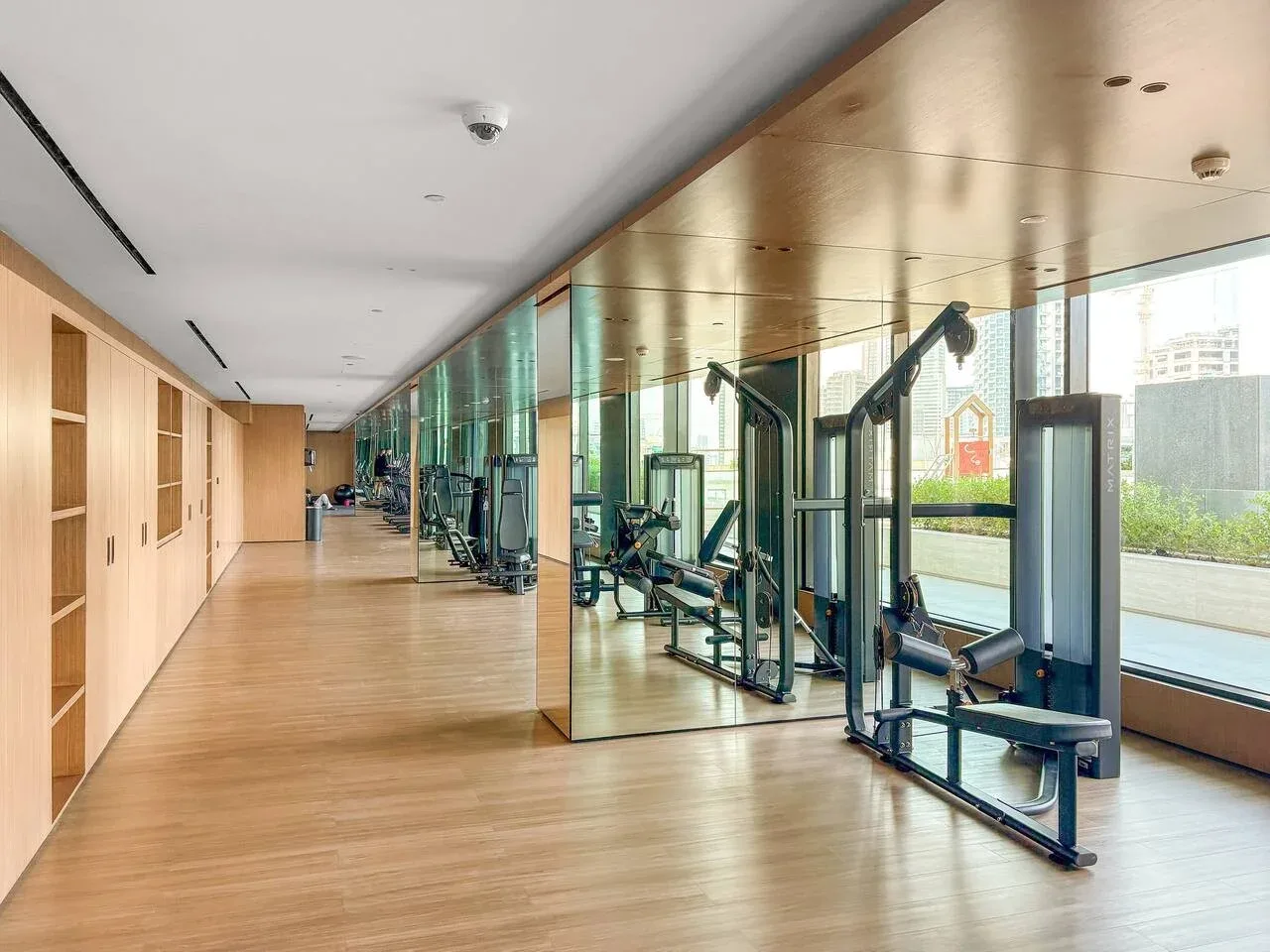 Una sala de ejercicio luminosa tiene máquinas junto a una pared de ventanas.