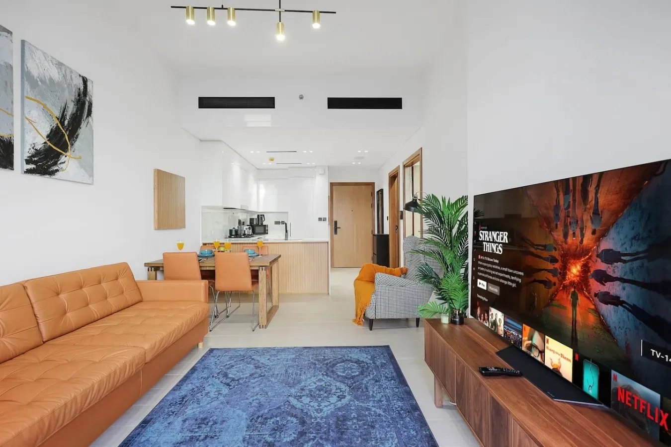 Una sala luminosa con sofá color canela, alfombra azul y televisor.