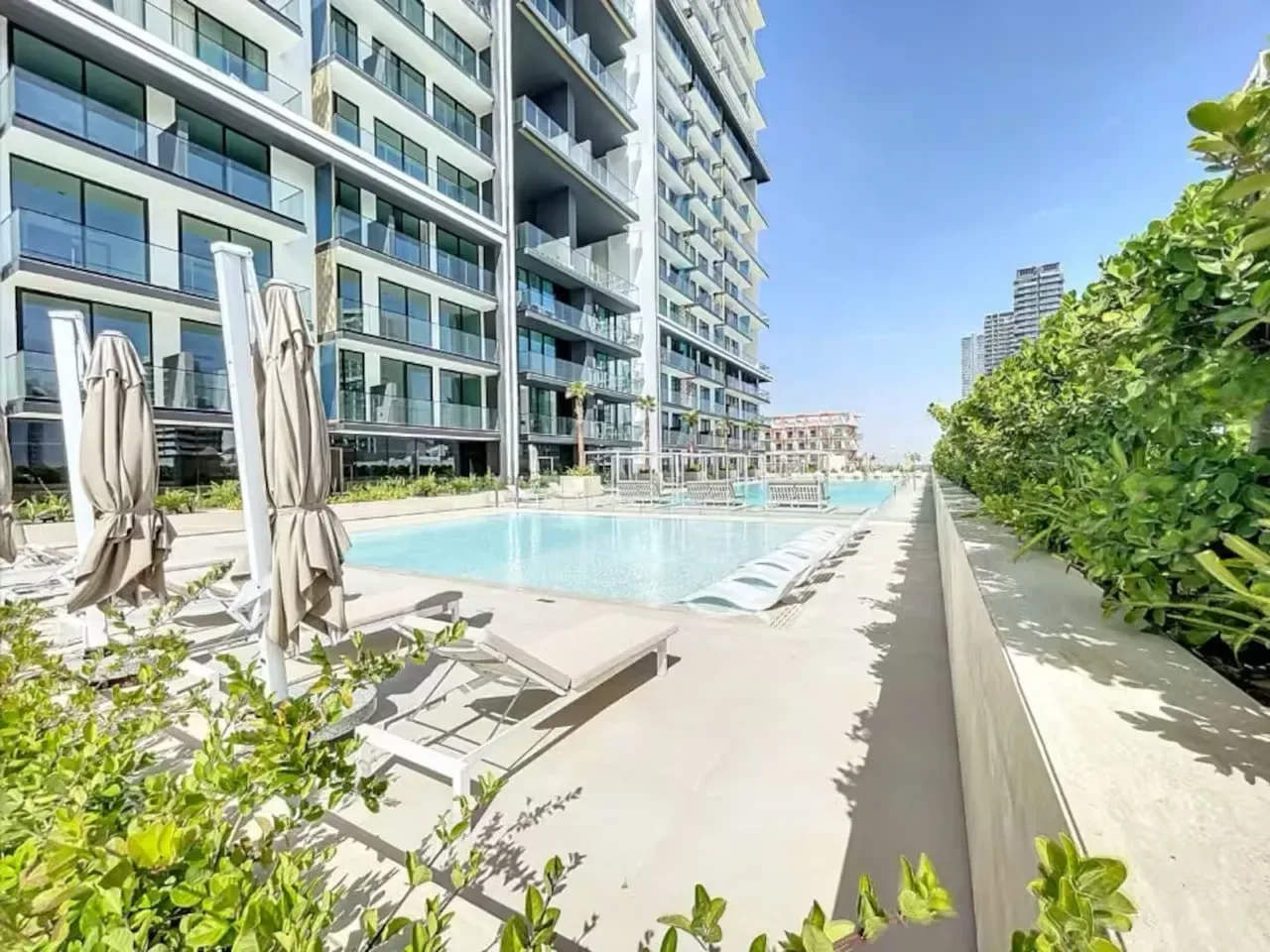 Una piscina al aire libre junto a un edificio moderno, con tumbonas alrededor.