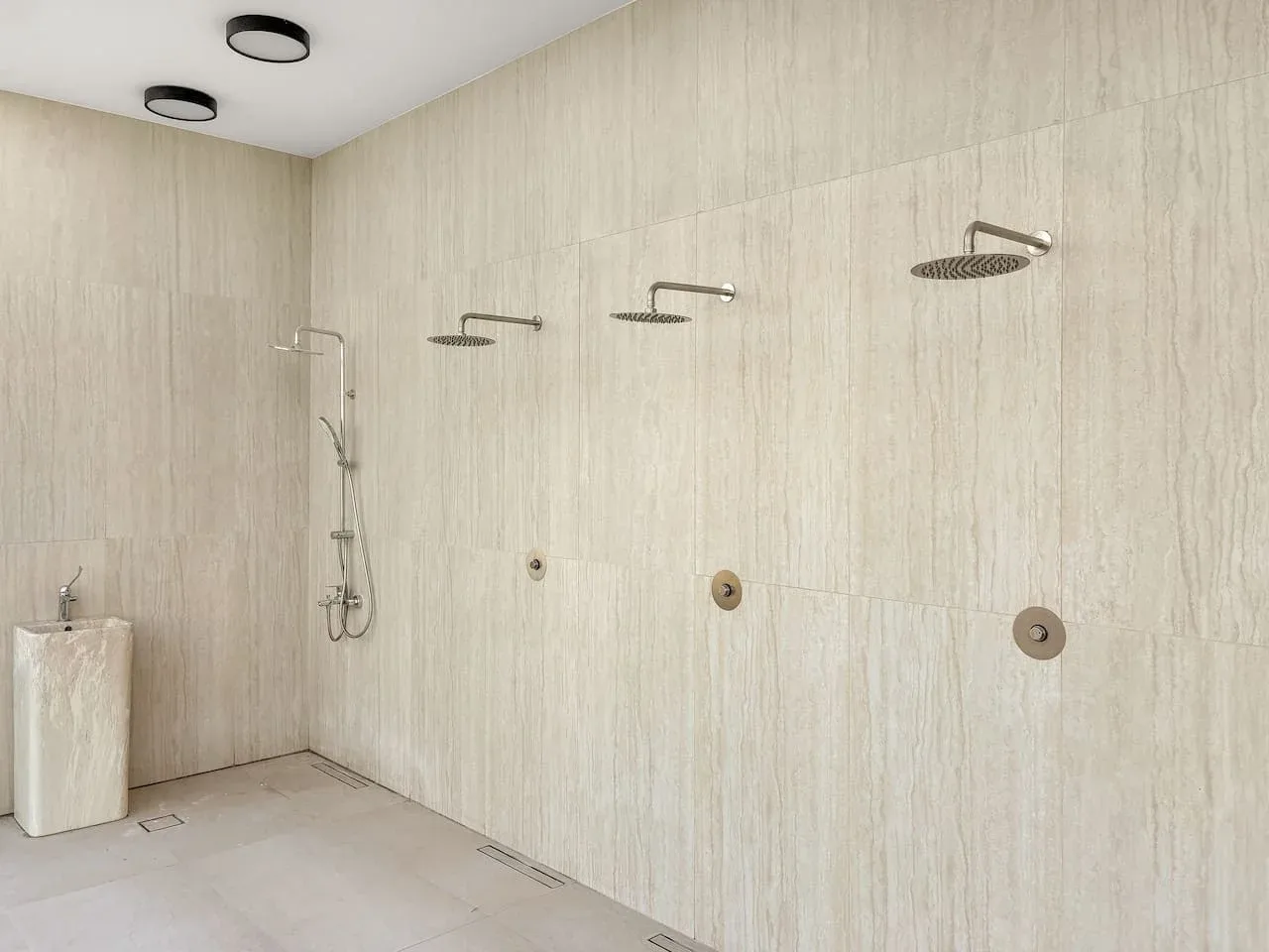 Un baño con ducha revestido de azulejos y varios cabezales en la pared.