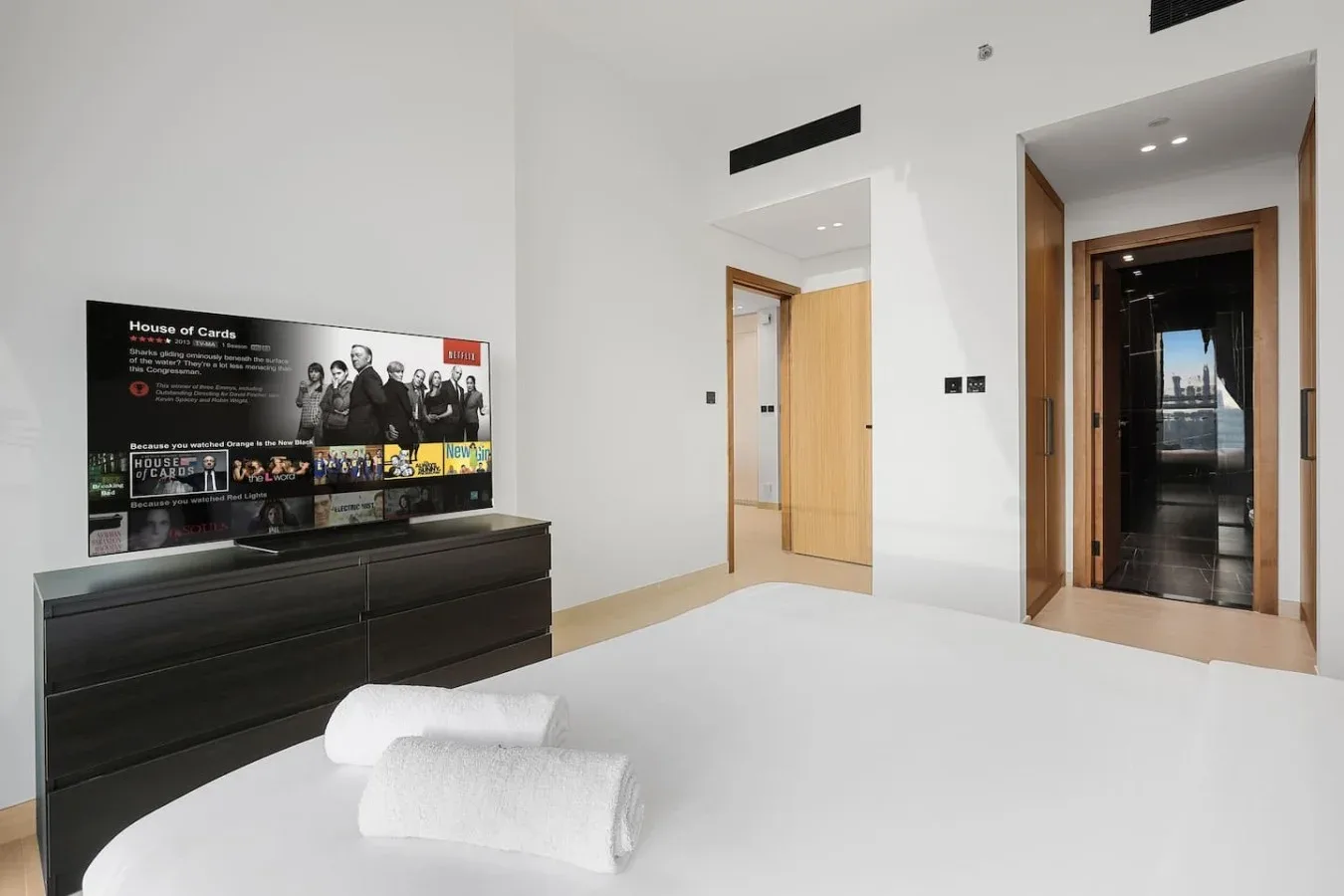Un dormitorio con ropa de cama blanca, una cómoda oscura y un televisor.