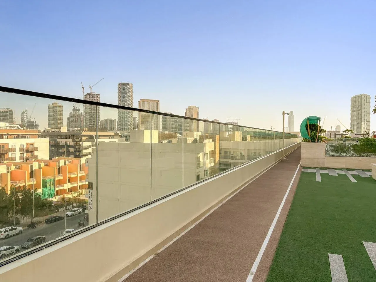 Una terraza en la azotea con un sendero estrecho y césped artificial mira hacia edificios de la ciudad.