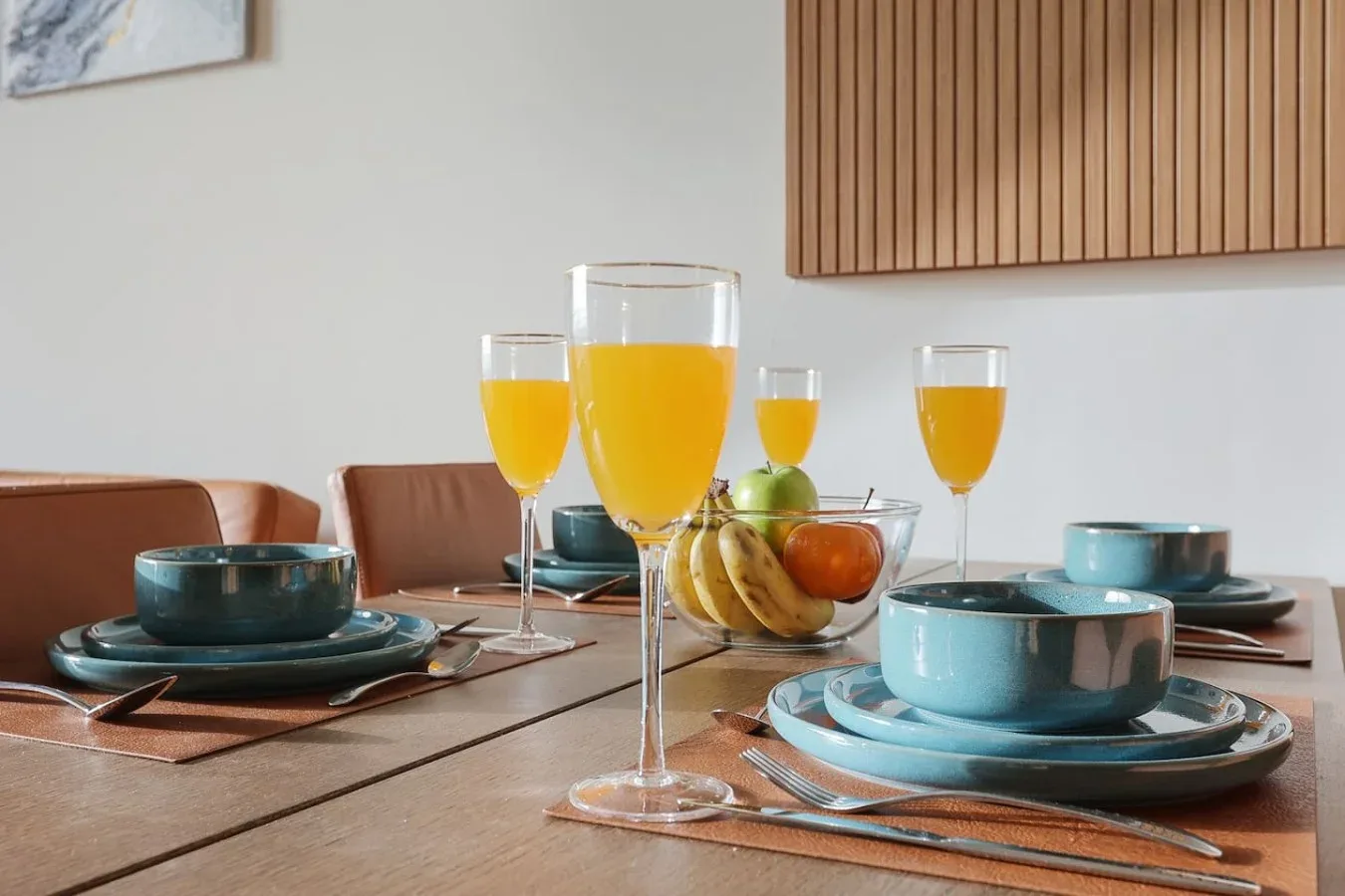 Una mesa de comedor está puesta con platos azules, fruta y vasos de jugo de naranja.