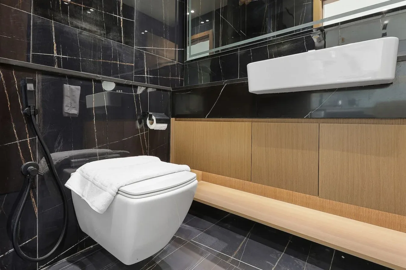 Un baño moderno con inodoro, lavabo de pared y paredes de azulejos oscuros.