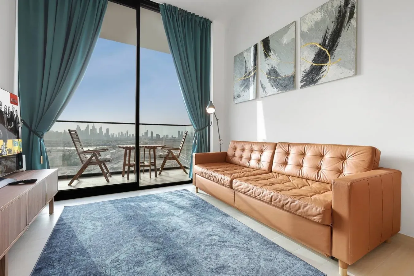 Una sala de estar con un sofá color canela, cortinas turquesa y una gran ventana con vistas a la ciudad.