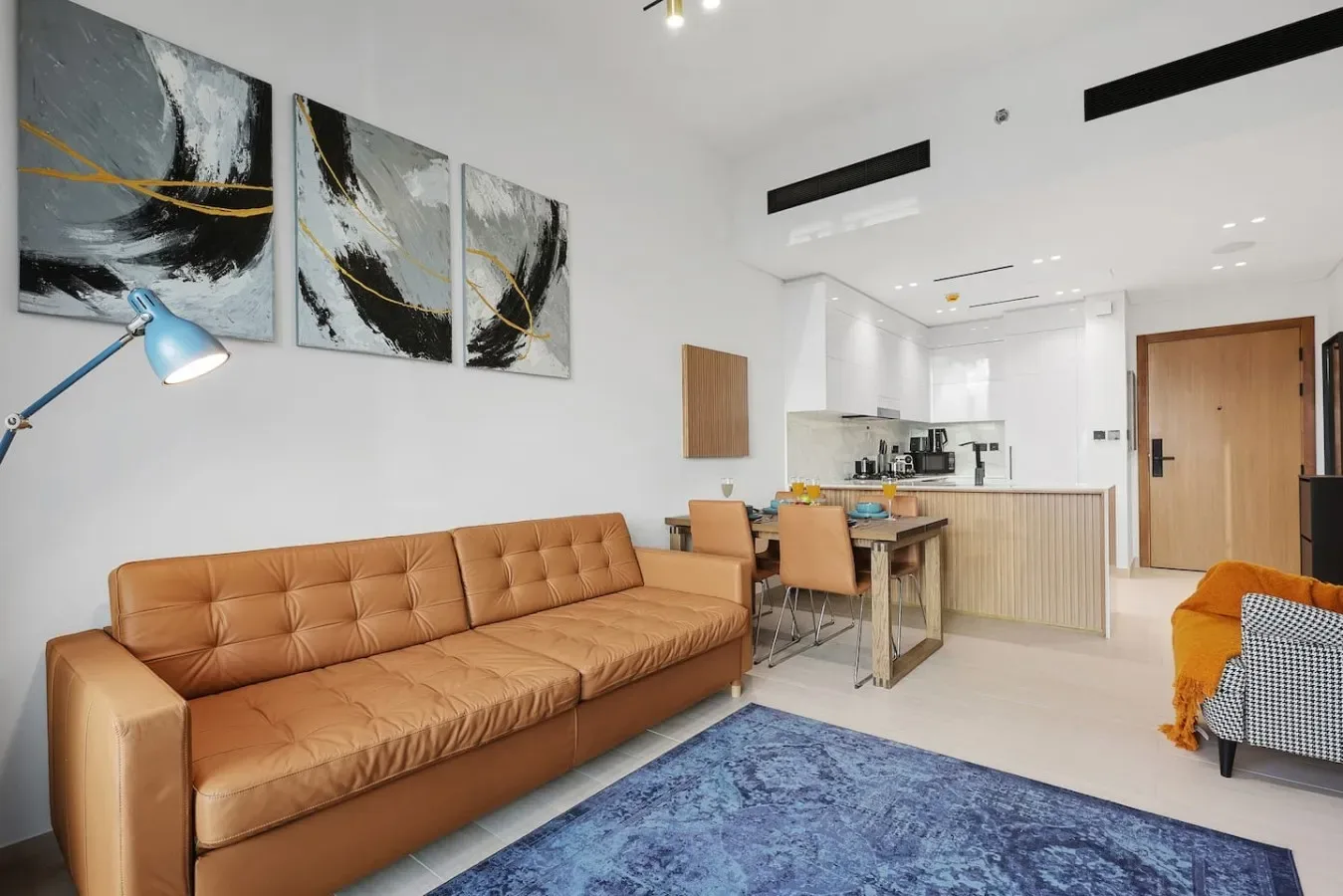 Una sala luminosa con un sofá color canela y una cocina abierta.
