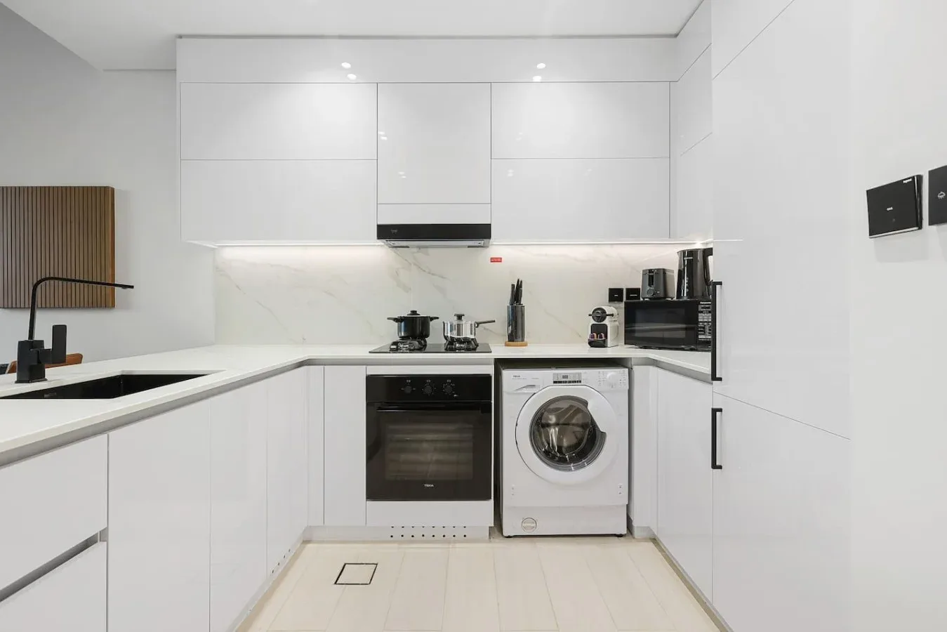 Una cocina blanca y luminosa con horno, lavadora y electrodomésticos sobre la encimera.