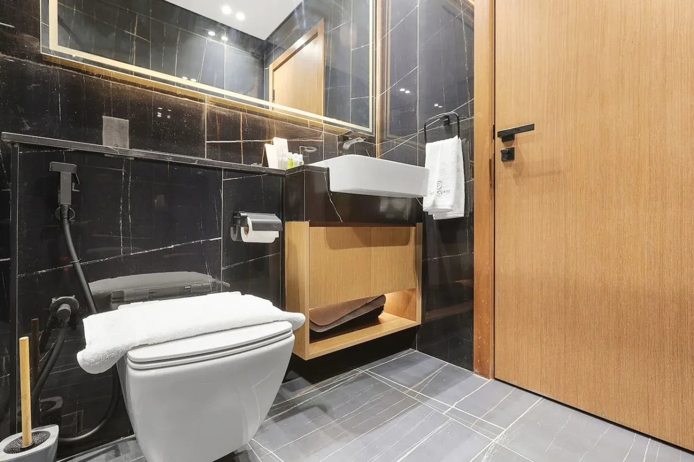 Un baño moderno con inodoro, lavabo suspendido y paredes de azulejos oscuros.