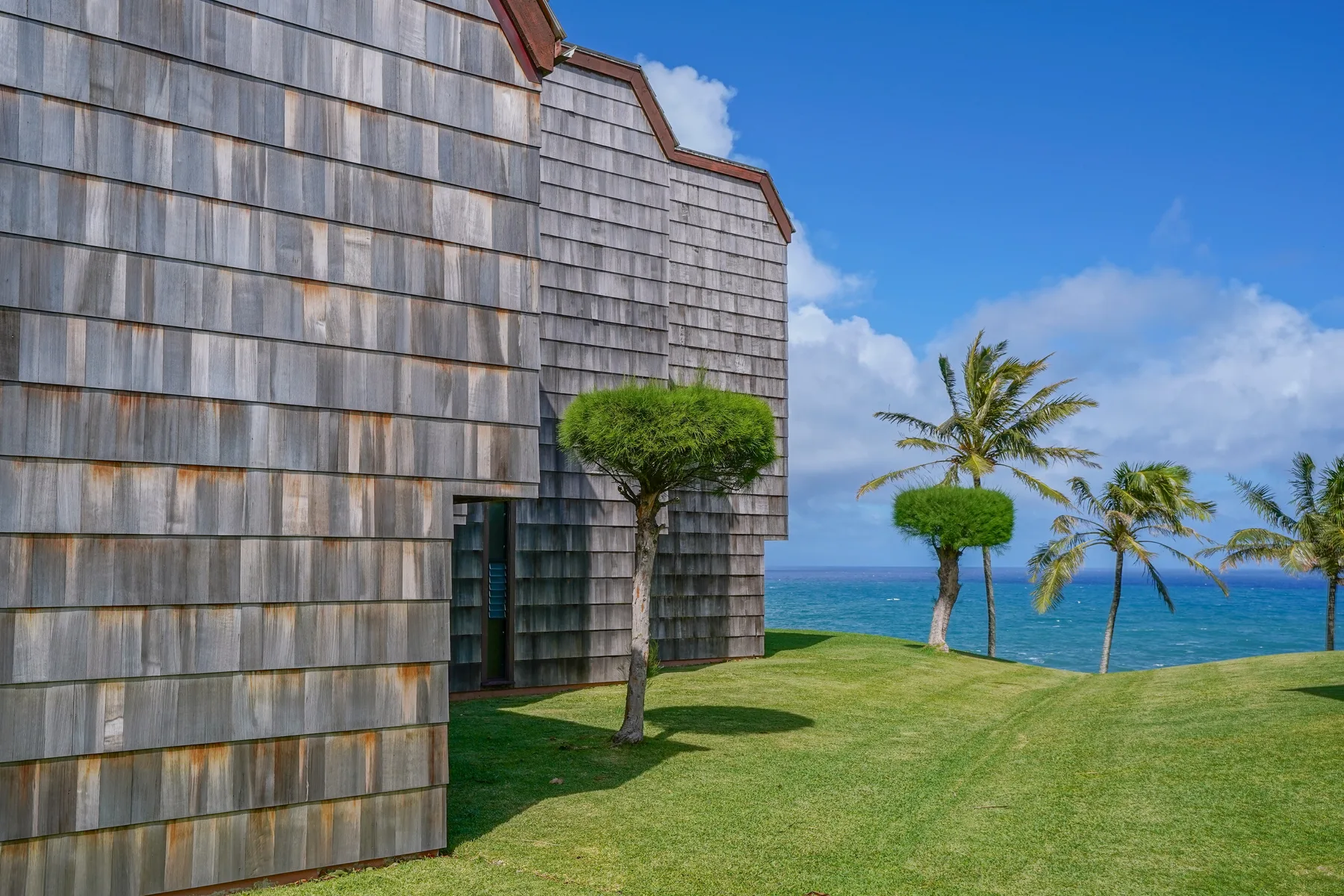 A shingled building stands beside a grassy lawn overlooking the ocean.