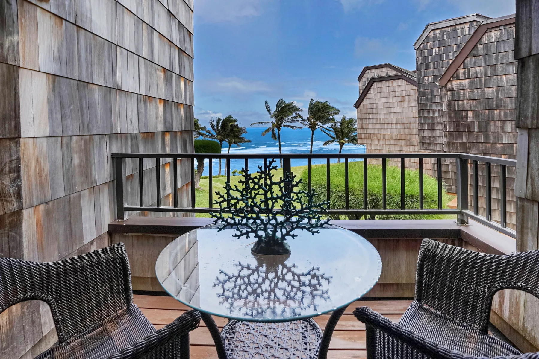 A balcony seating area overlooks palm trees and the ocean.