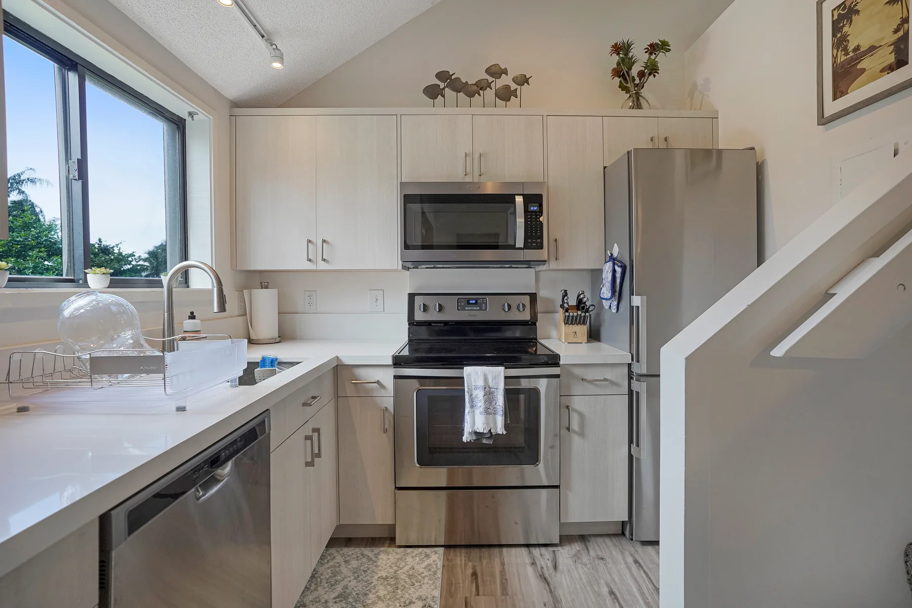 A bright kitchen with white cabinetry, stainless steel appliances, and a large window.