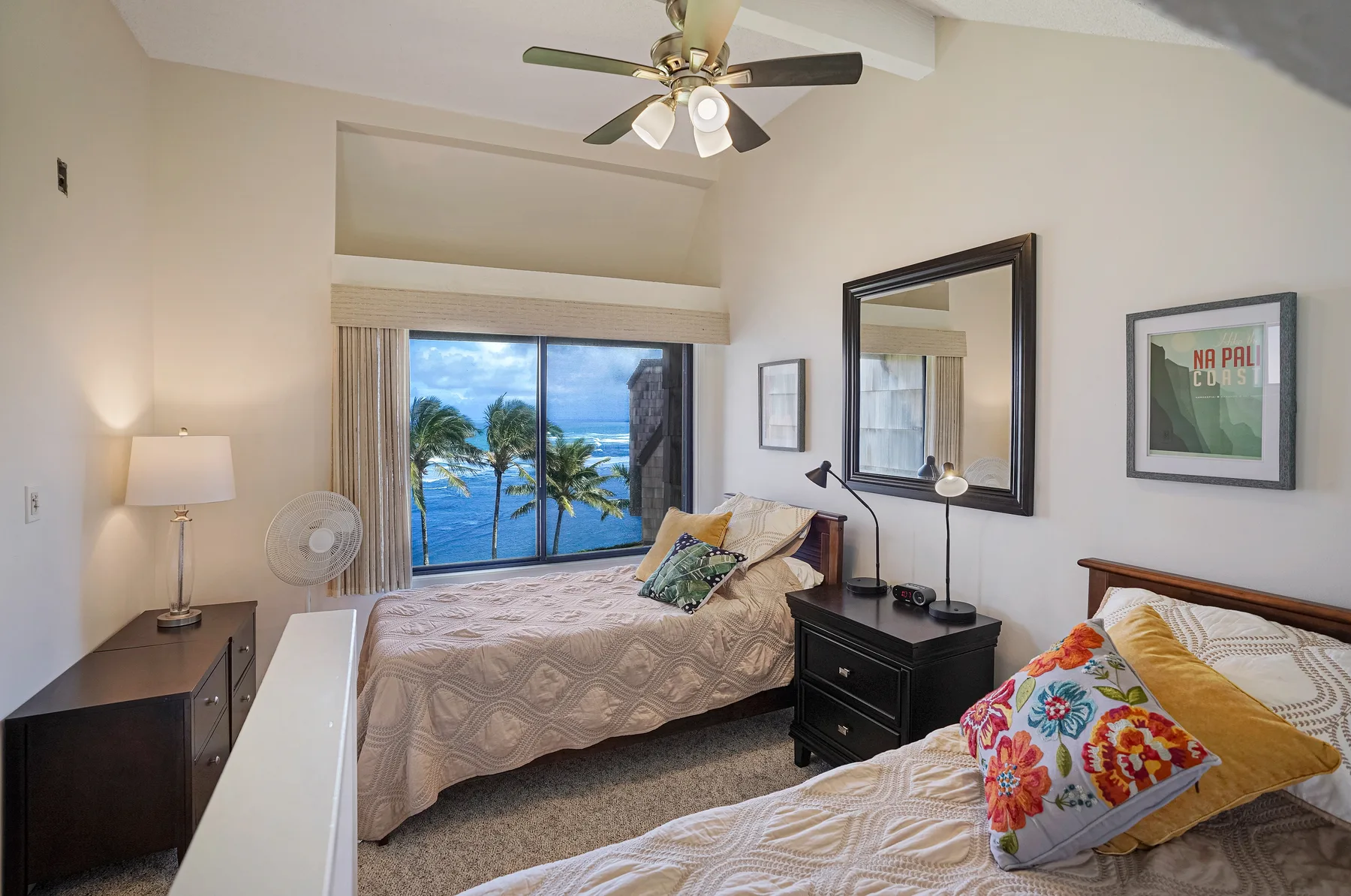 A bedroom with two beds, a ceiling fan, and a large window overlooking palm trees and water.