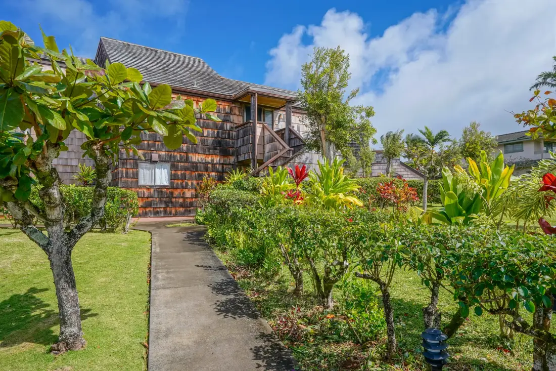 A garden path leads toward a shingled building amid flowering plants.