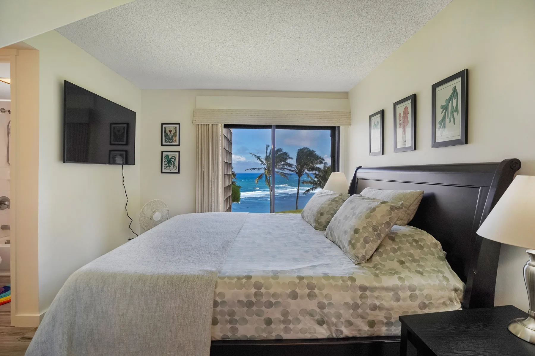 A bedroom with a large bed facing a window overlooking the ocean.