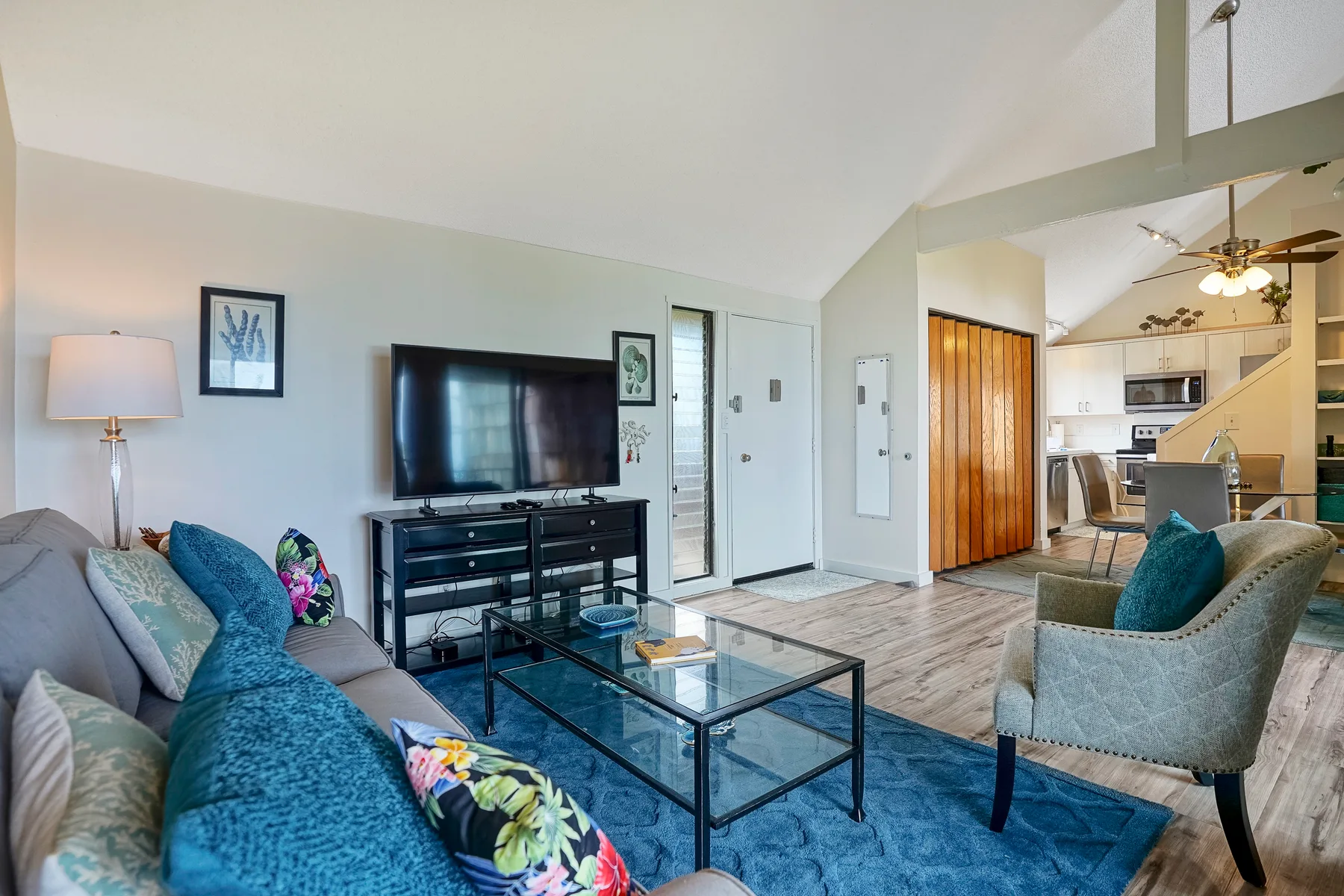 A living room with seating, a television, and an open kitchen beyond.