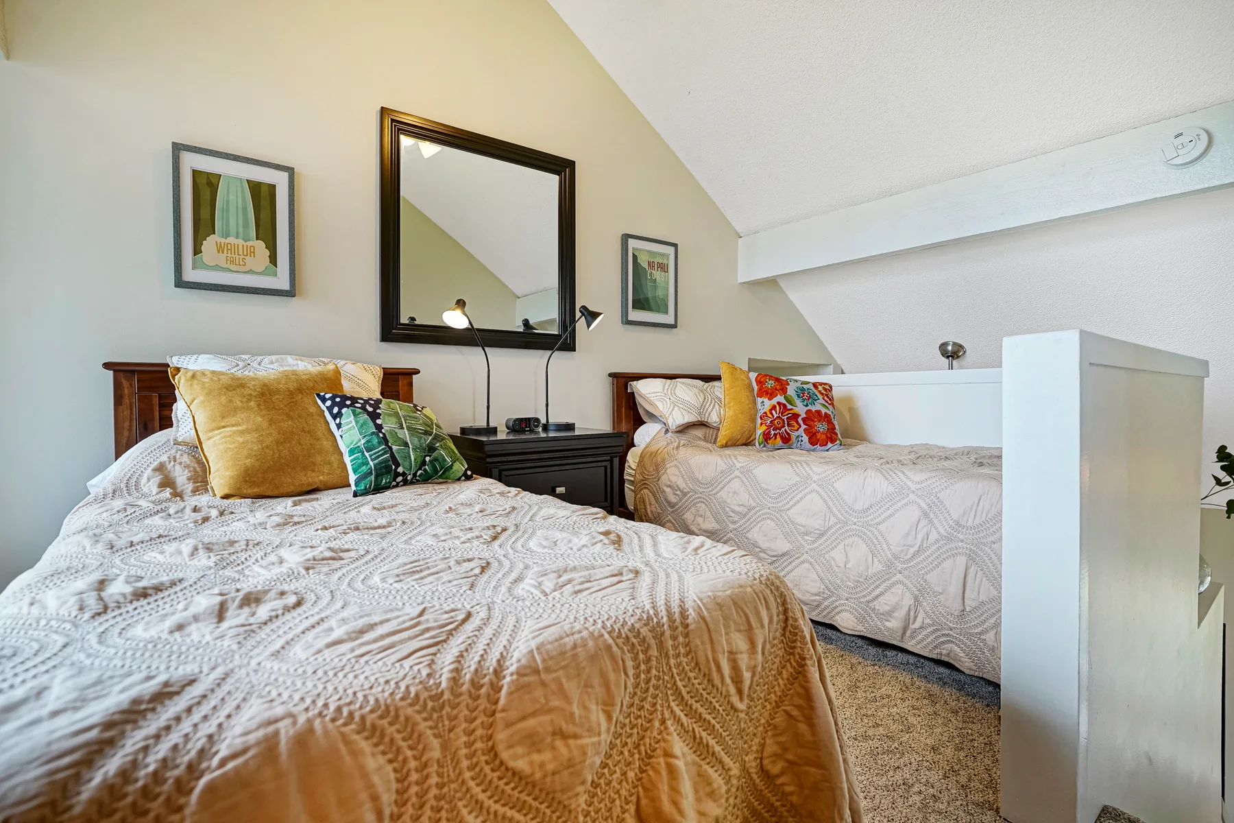 A bedroom with two beds, patterned bedding, and framed wall art.