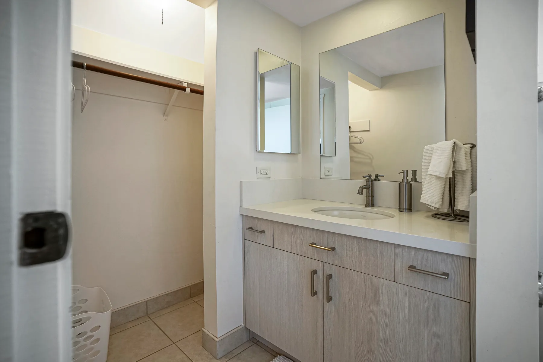 A bathroom vanity with a sink and mirror stands beside an open closet.
