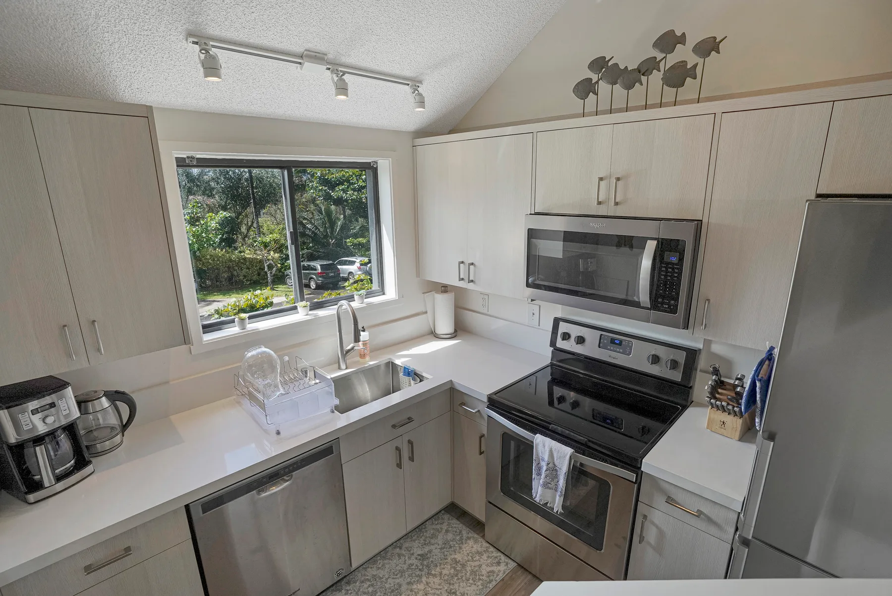 A bright kitchen with pale cabinets, a sink, and a stainless steel stove.