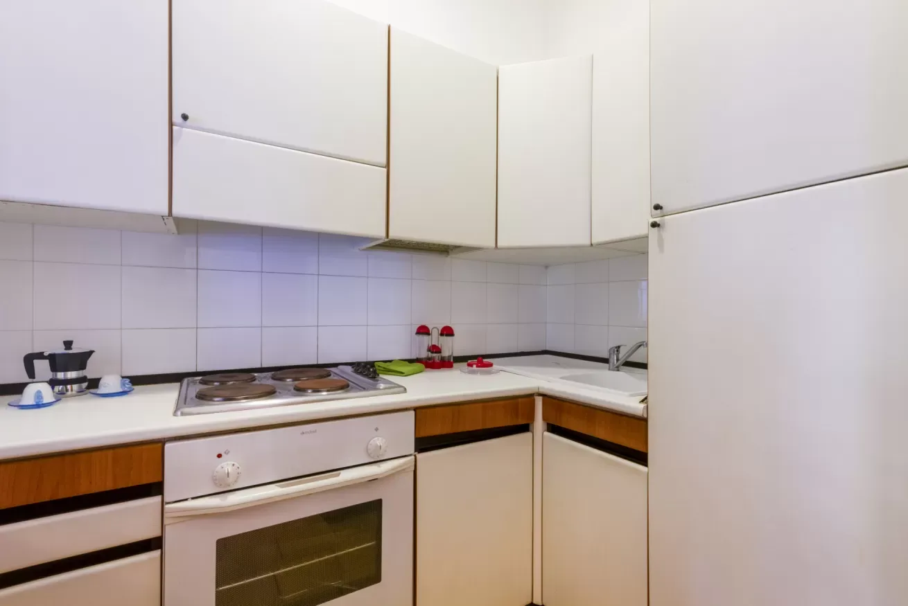 Una cocina compacta con estufa, horno y gabinetes blancos.