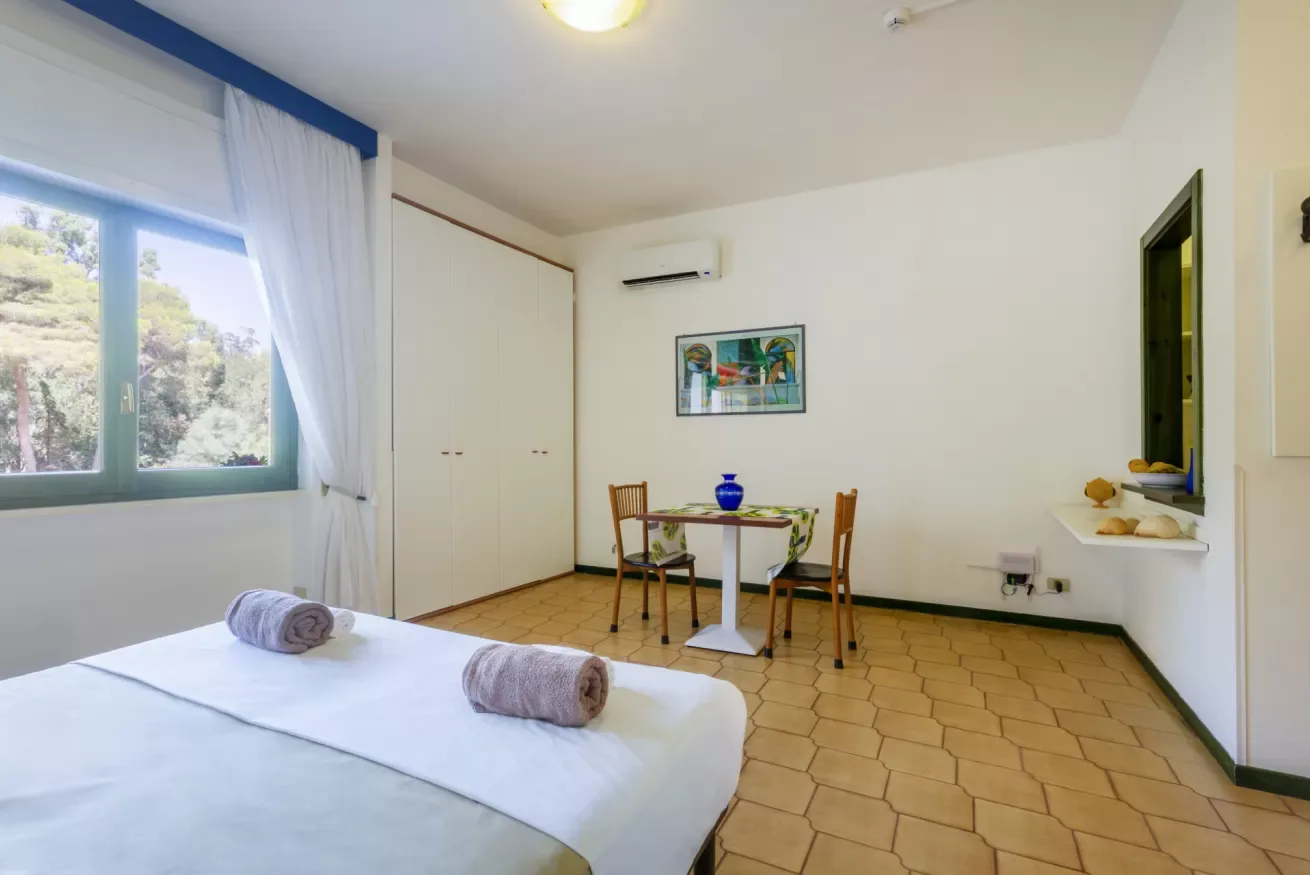 Un dormitorio con una cama, una pequeña mesa de comedor y una ventana con cortinas.