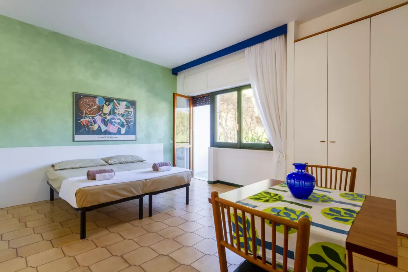 Un dormitorio luminoso con una cama, una ventana y una pequeña mesa de comedor.