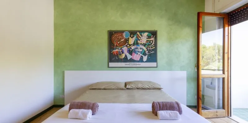 Un dormitorio con una cama bajo un cuadro colorido y una puerta de cristal abierta.