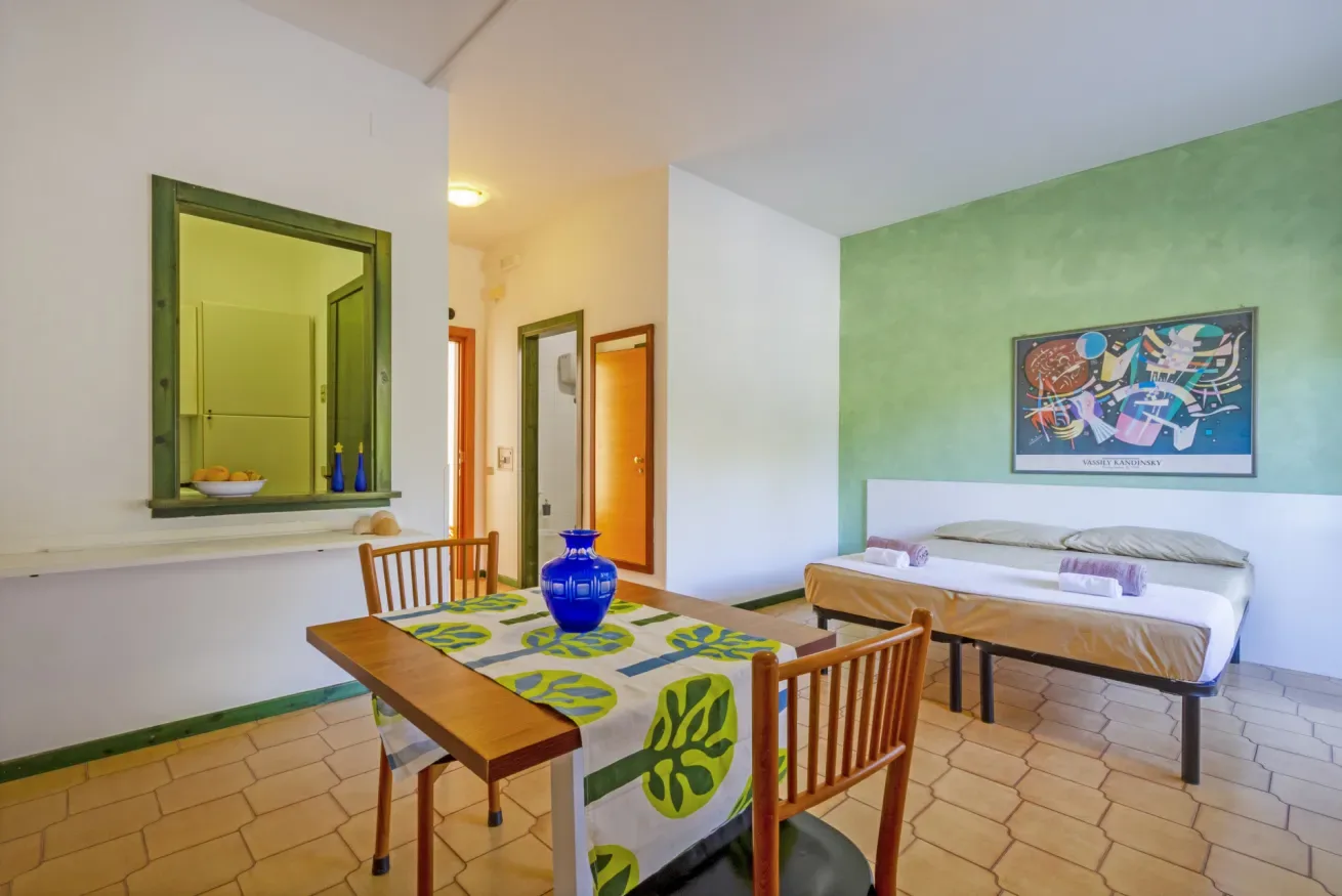 Una habitación luminosa con una mesa de comedor de madera junto a una cama y una pared verde.
