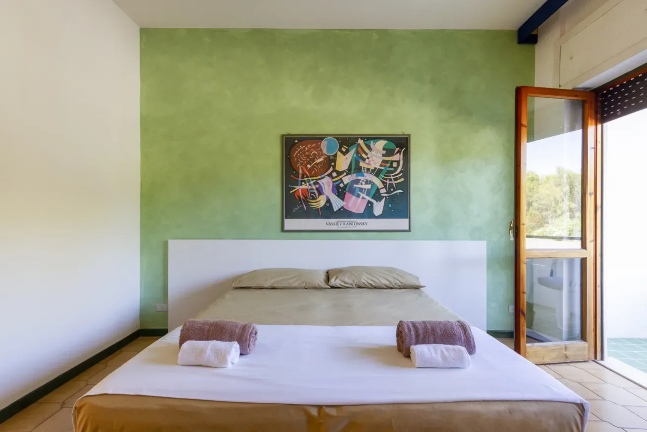 Un dormitorio con una cama frente a una pared verde y una puerta abierta al balcón.
