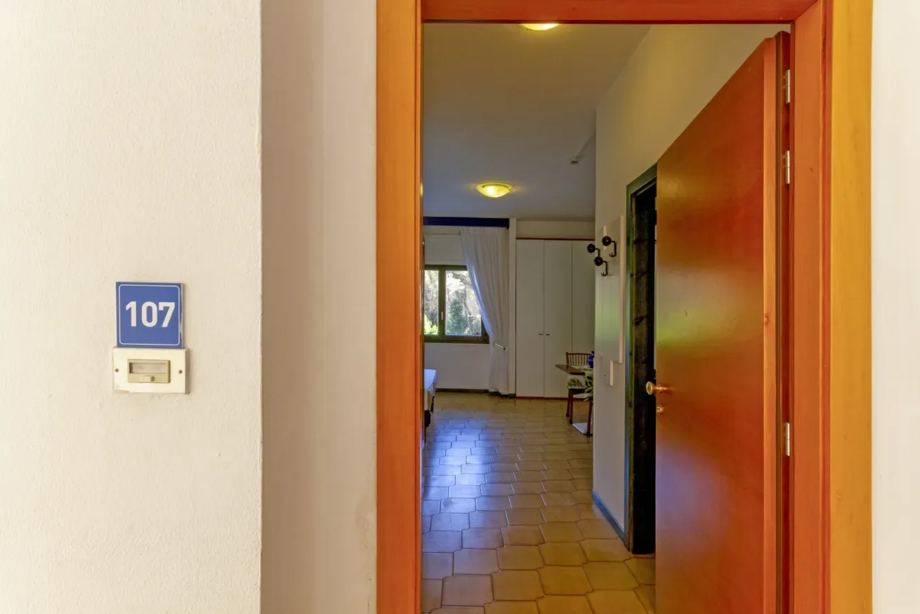 Una puerta da a un pasillo interior con suelo de baldosas y una ventana al fondo.
