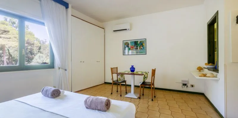 Un dormitorio con una cama, una mesa pequeña, sillas y una ventana.
