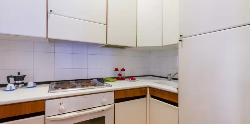 Una cocina con azulejos, gabinetes blancos y una estufa sobre la encimera.