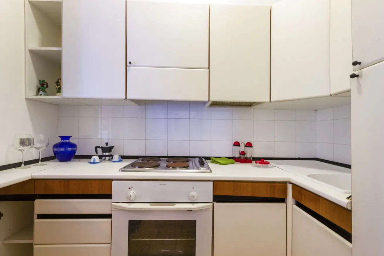 Una cocina con gabinetes blancos, paredes de azulejos y una estufa.