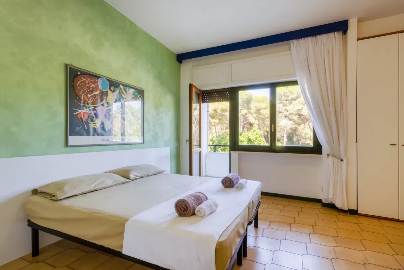 Un dormitorio con una cama junto a una ventana grande con vistas a la vegetación.