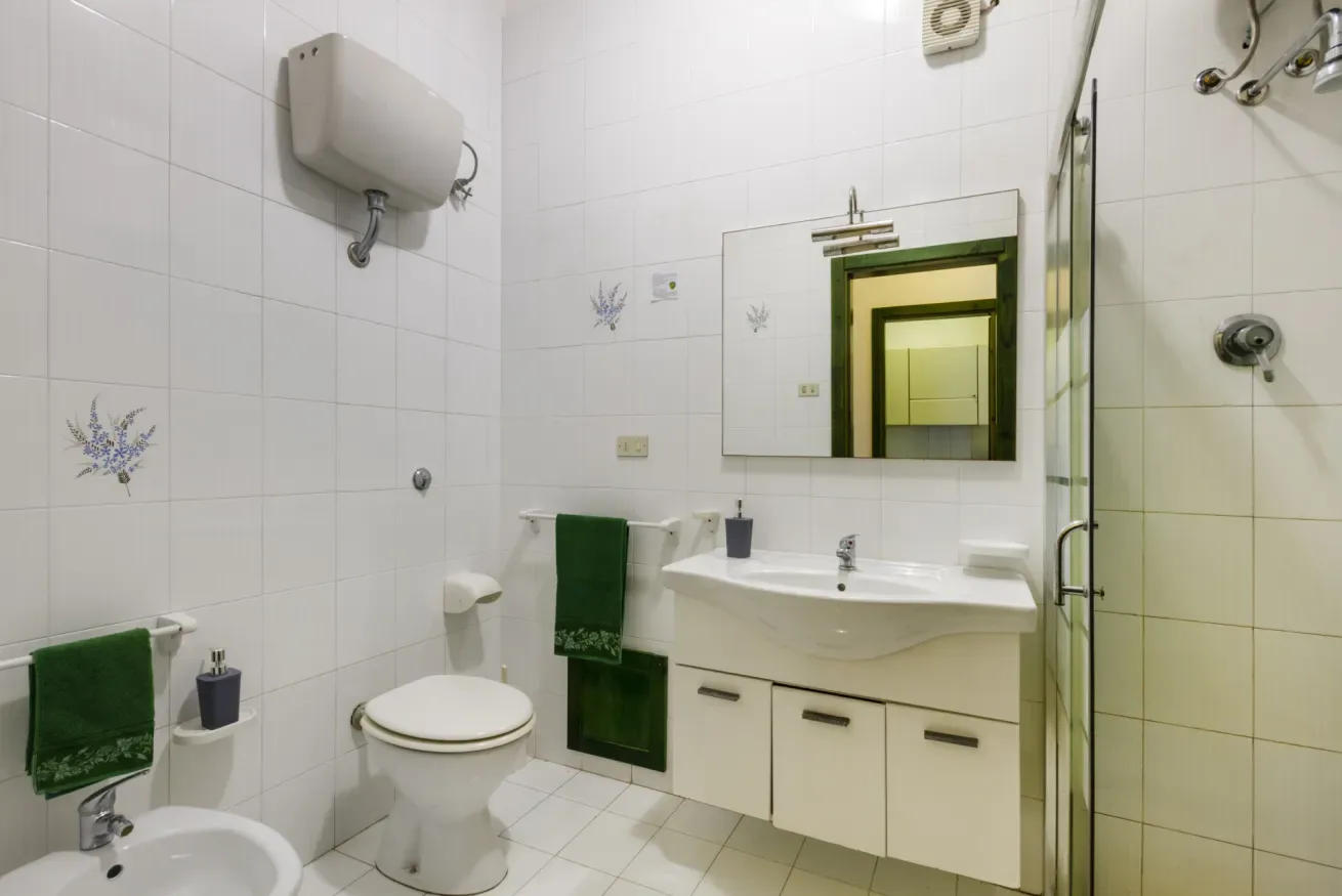 Un baño alicatado con lavabo, espejo e inodoro.