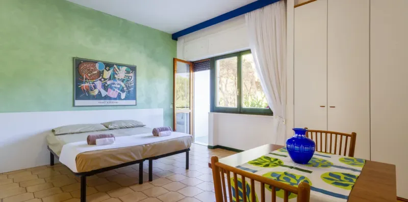 Un dormitorio con una cama, un armario y una mesa pequeña junto a la ventana.