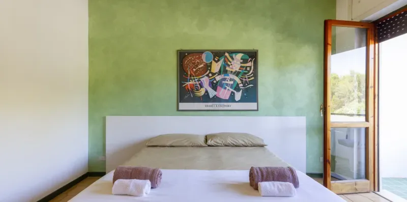 Un dormitorio con una cama junto a una pared verde y una puerta abierta al balcón.