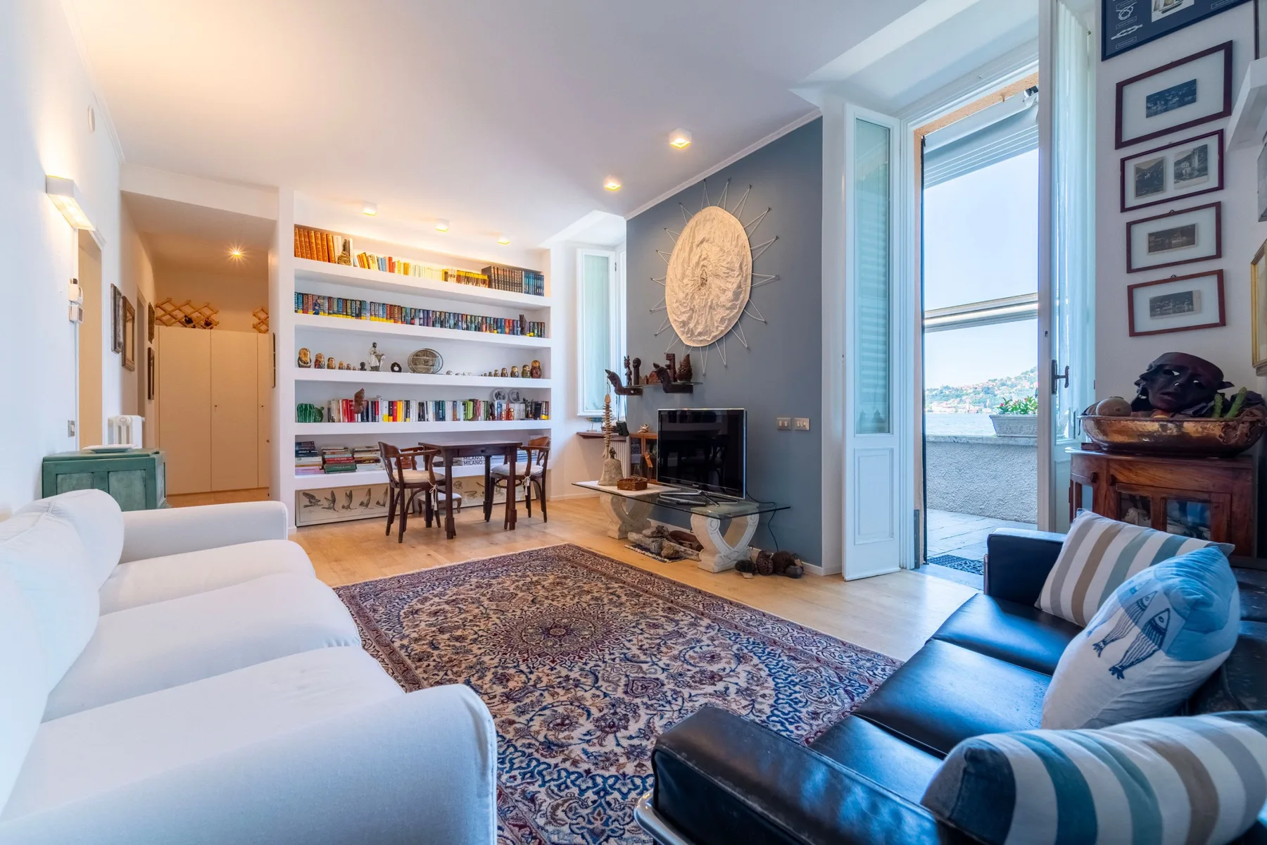 A bright living room with a patterned rug and a dining table beside built-in shelves.