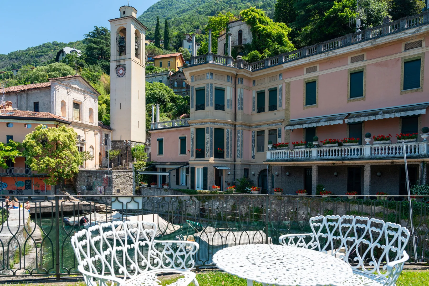 An outdoor terrace with ornate white seating overlooks pastel buildings and a bell tower.
